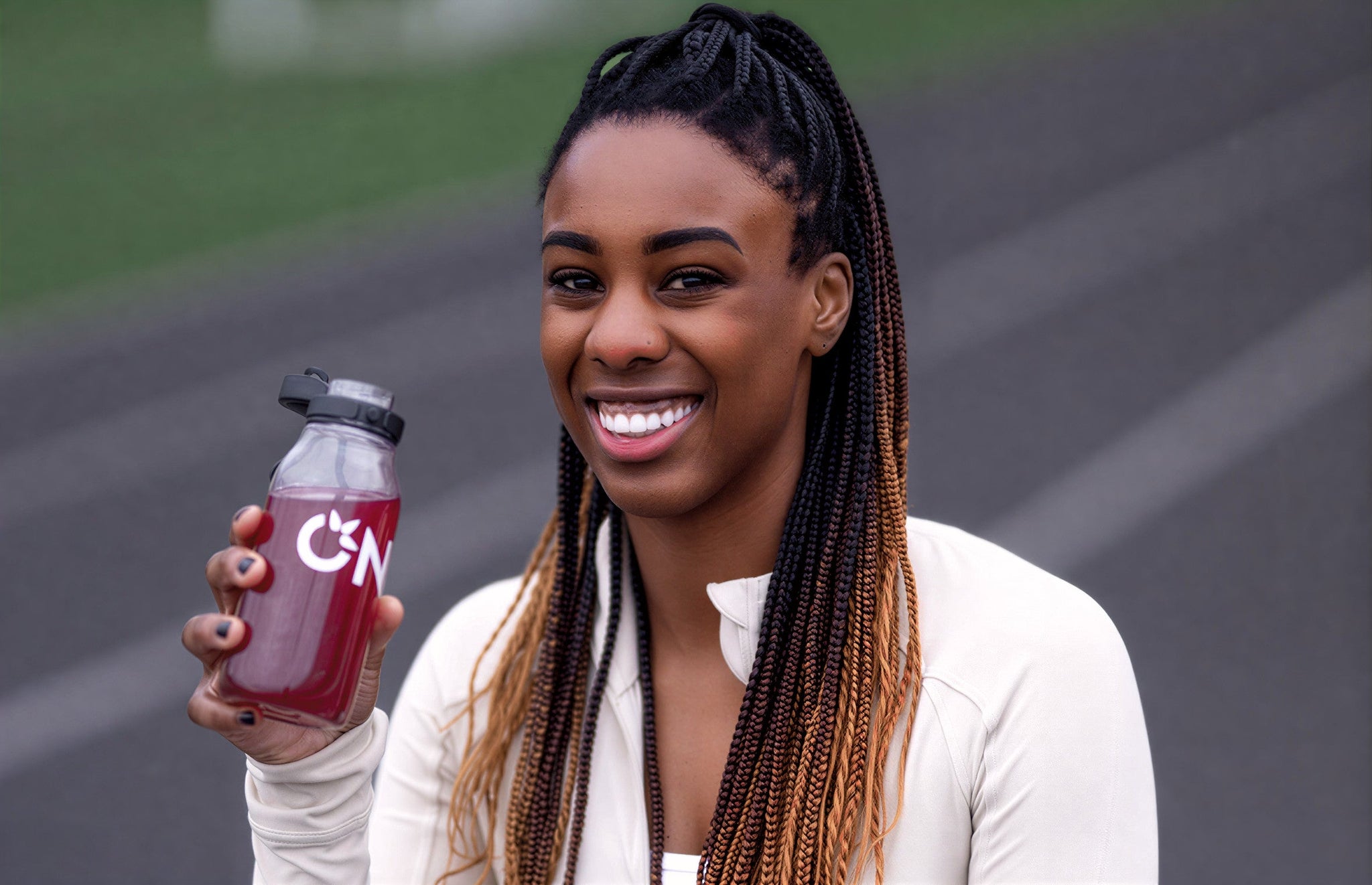 A woman with braids holds a bottle of juice, illustrating hydration tips related to electrolyte use.
