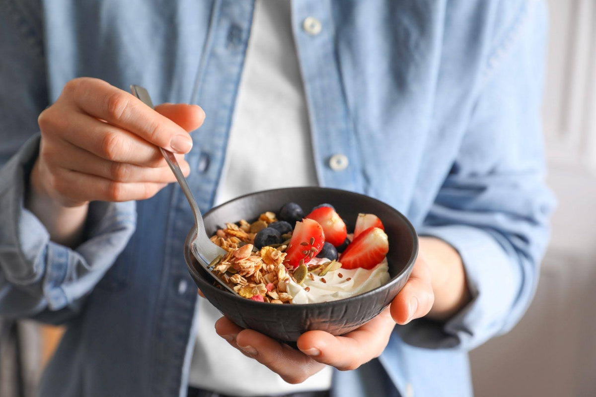 A hand grasping a bowl of granola topped with colorful fruit representing a nutritious meal choice