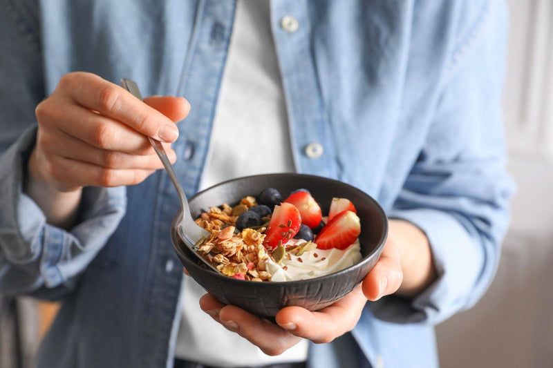 A hand grasping a bowl of granola topped with colorful fruit representing a nutritious meal choice