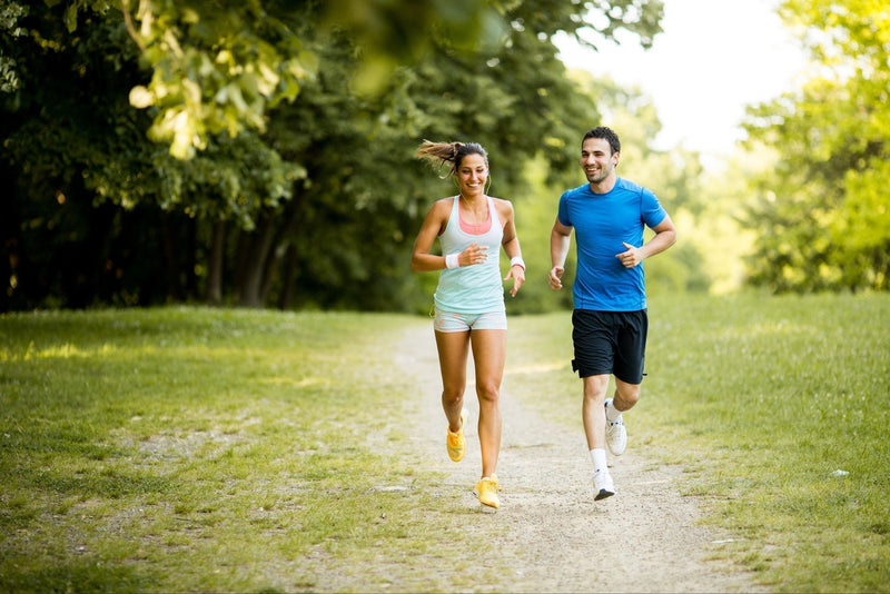 Two people running on a path in a park with trees in the background
