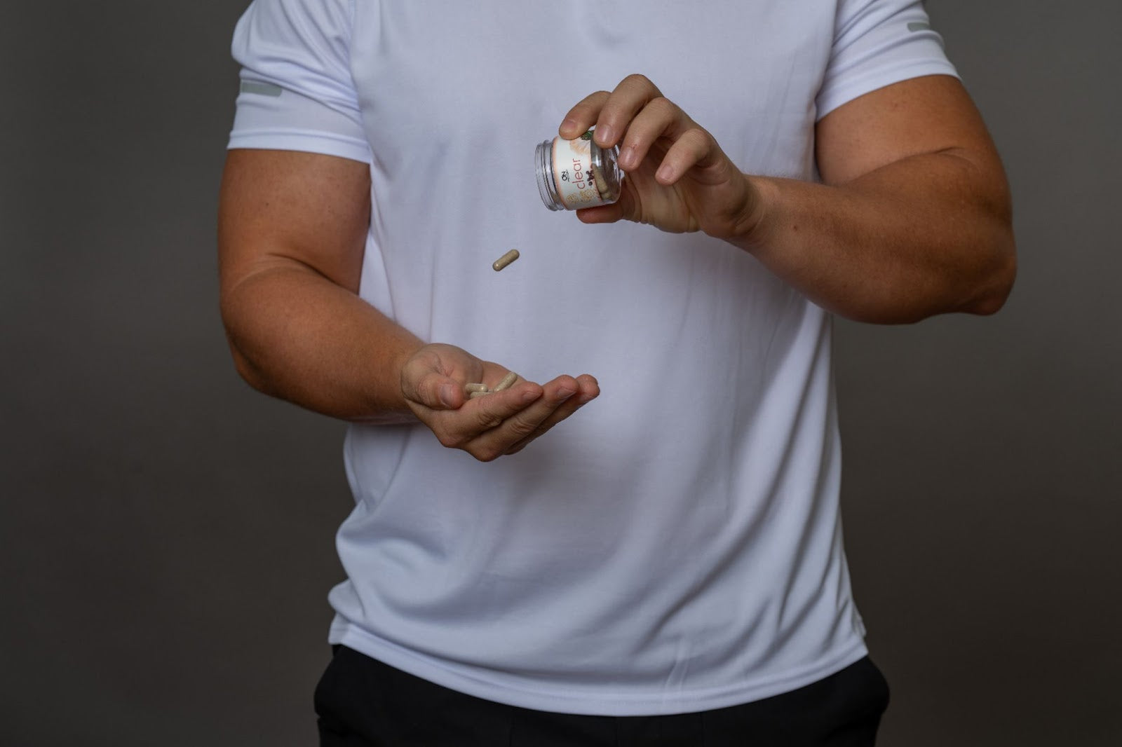 A man in a white athletic shirt pouring supplement capsules into his hand.