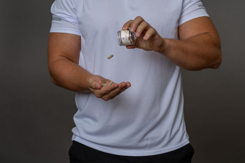 A man in a white athletic shirt pouring supplement capsules into his hand.