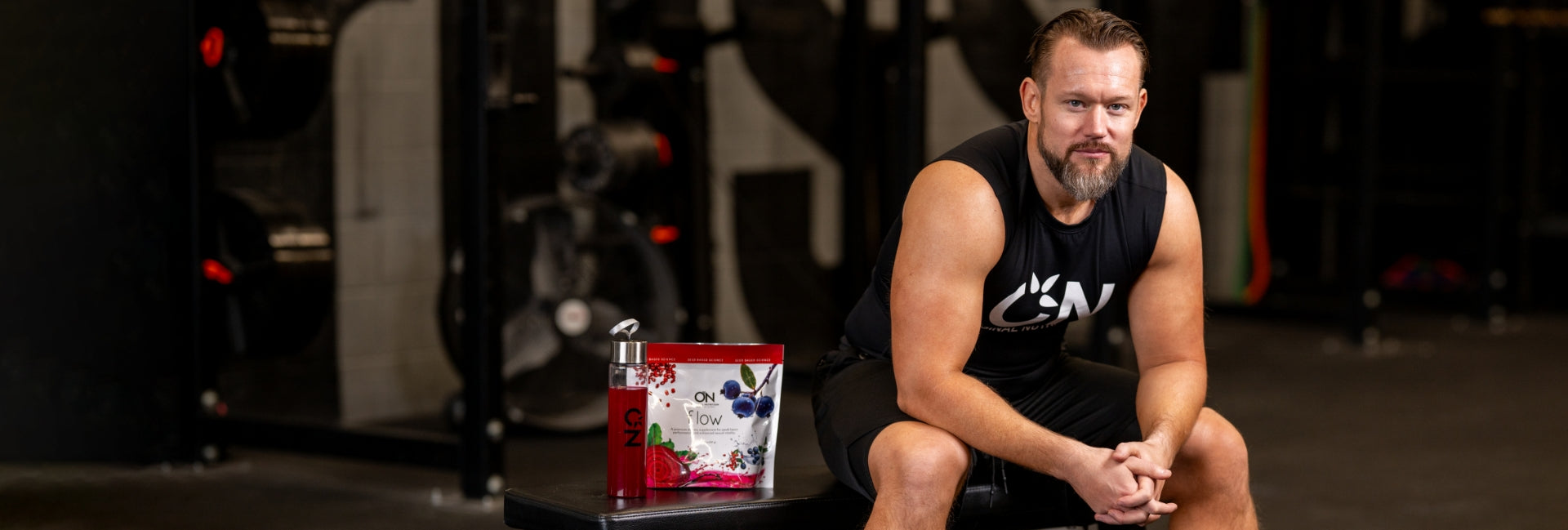 Man sitting on a bench in a gym with a supplement container in front of him