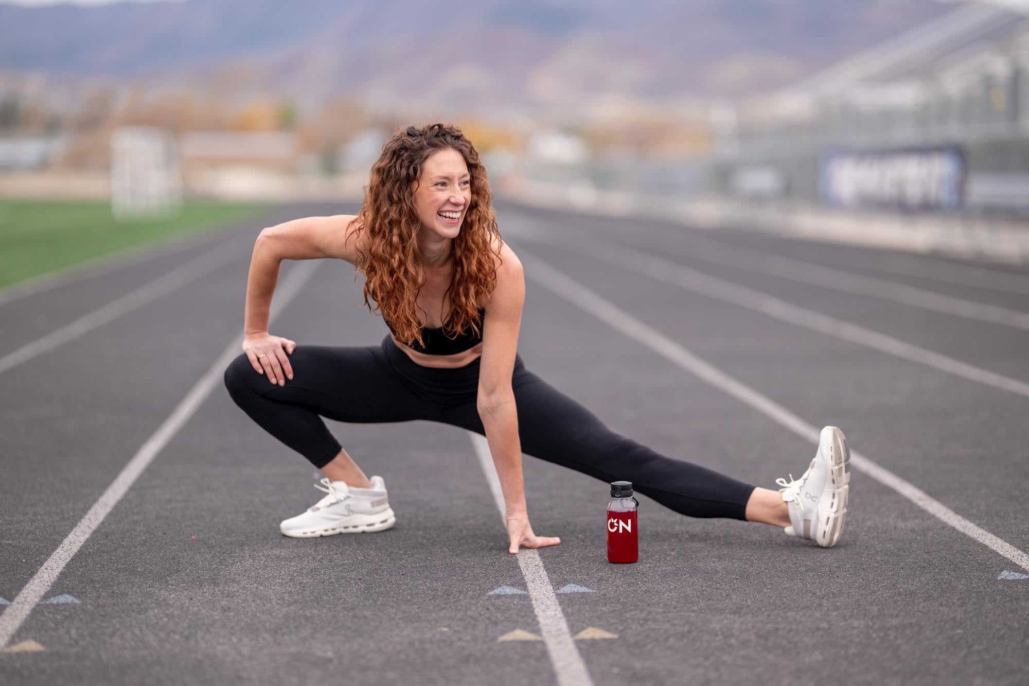 Woman stretching on a track with a water bottle nearby